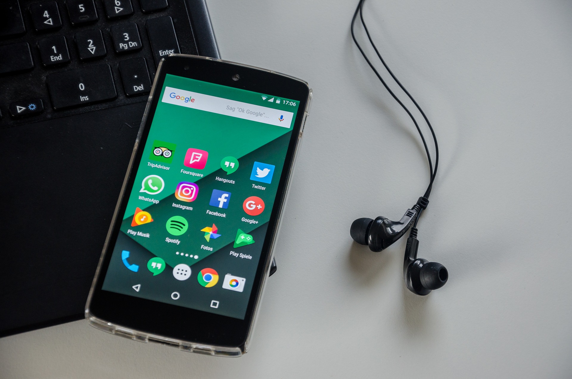 Das Bild zeigt ein Smartphone mit Apps sowie eine Tastatur und Kopfhörer.