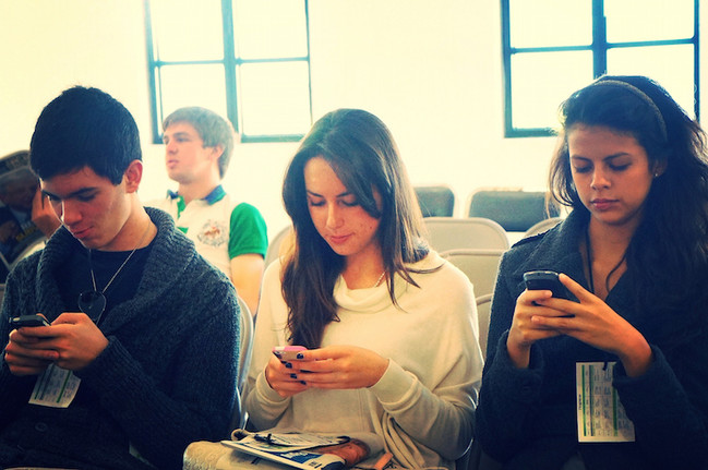 Drei junge Menschen sitzen nebeneinander und nutzen ihre Smartphones