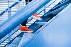 Bild: Treppe Das Bild zeigt die Füße und Beine einer Person, die eine Metalltreppe hinaufsteigt.
