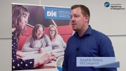 Das Bild zeigt einen Mann in einer Halbnah-Aufnahme, der mit einem nicht sichtbaren Interviewpartner zu sprechen scheint. Im Hintergrund befindet sich ein Roll-up vom Deutschen Institut für Erwachsenenbildung.