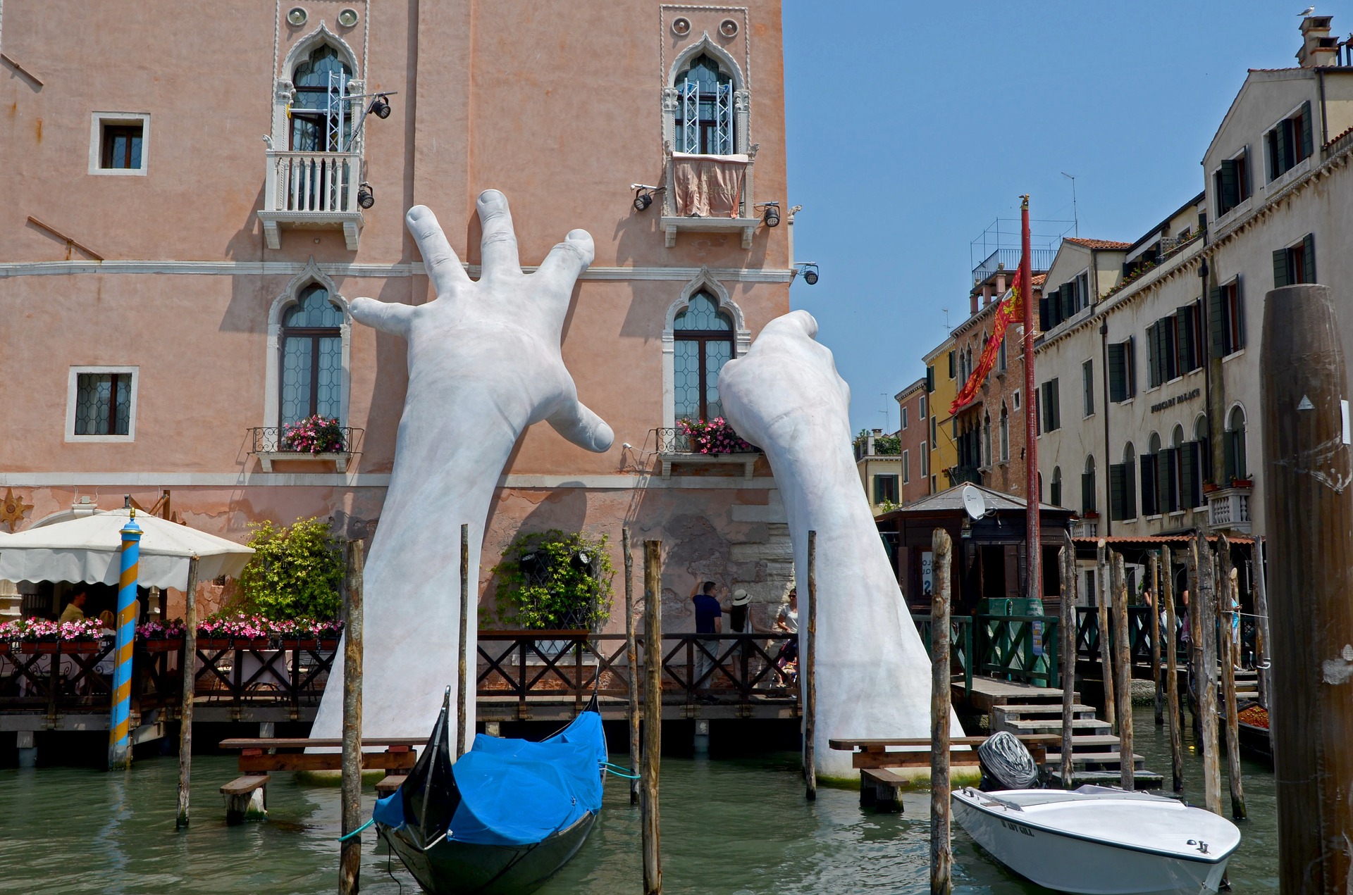 Das Bild zeigt, wie zwei riesige Hände ein Haus in Venedig stützen.