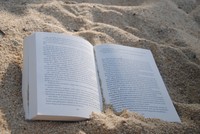 Das Bild zeigt ein aufgeschlagenes Buch, das im Sand liegt. 